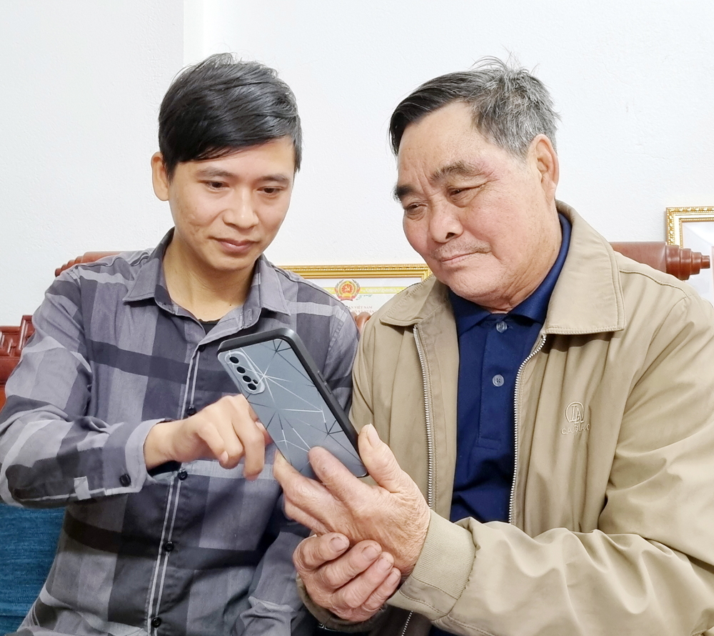 Đồng chí Bùi Duy Tuấn (bên trái) hướng dẫn người dân cài đặt, kích hoạt định danh điện tử.